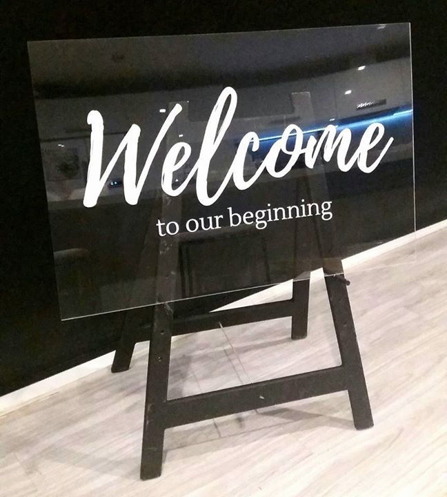 Acrylic sign with 'Welcome to our beginning' text on a stand against a black background.